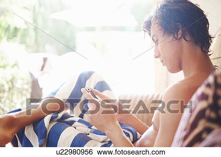Young man wrapped in towel reading smartphone texts on patio chair View Large Photo Image Stock Photograph - Young man wrapped in towel reading smartphone texts on patio chair. Fotosearch