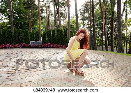 Stock Photo - Young woman adjusting shoe straps in park. Fotosearch
