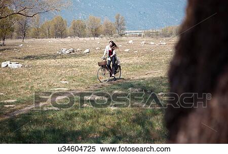 Stock Photography - Young woman cycling along rural track. Fotosearch