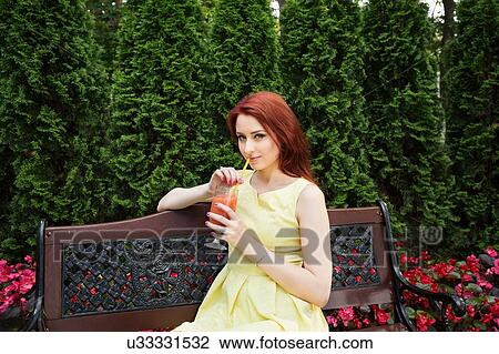 Young woman drinking juice on park bench View Large Photo Image Stock Image - Young woman drinking juice on park bench. Fotosearch