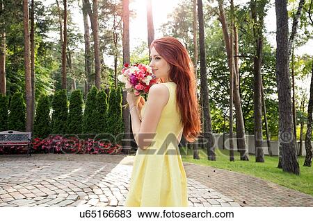 Stock Image - Young woman holding bunch of flowers in park. Fotosearch