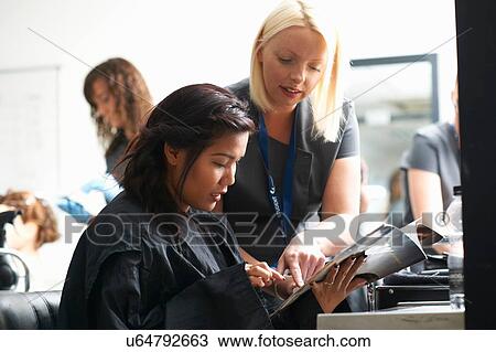 Young woman in hair salon wearing hair cutting cape choosing hairstyle from magazine View Large Photo Image Stock Image - Young woman in hair salon wearing hair cutting cape choosing hairstyle from magazine. Fotosearch