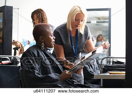 Stock Photo - Young woman in hair salon wearing hair cutting cape choosing hair dye colour from swatches. Fotosearch