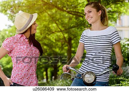 Young woman on bicycle talking to young woman wearing panama hat View Large Photo Image Stock Photo - Young woman on bicycle talking to young woman wearing panama hat. Fotosearch