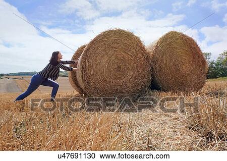 Young woman pretending to push haystacks in harvested field View Large Photo Image Stock Image - Young woman pretending to push haystacks in harvested field. Fotosearch