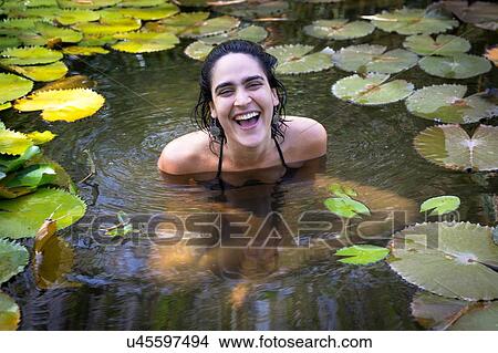 "Young woman surrounded by lily pads sitting in pond, looking at camera smiling" View Large Photo Image Picture - "Young woman surrounded by lily pads sitting in pond, looking at camera smiling". Fotosearch