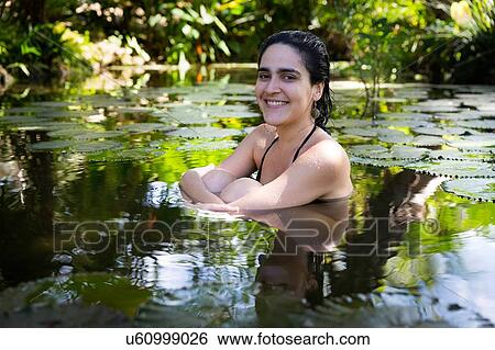 "Young woman surrounded by lily pads sitting in pond hugging knees, looking at camera smiling" View Large Photo Image Stock Photograph - "Young woman surrounded by lily pads sitting in pond hugging knees, looking at camera smiling". Fotosearch