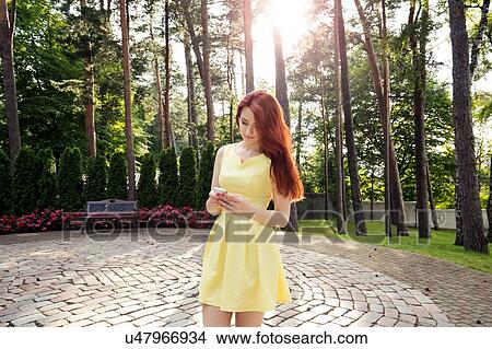 Picture - Young woman using smartphone in park. Fotosearch