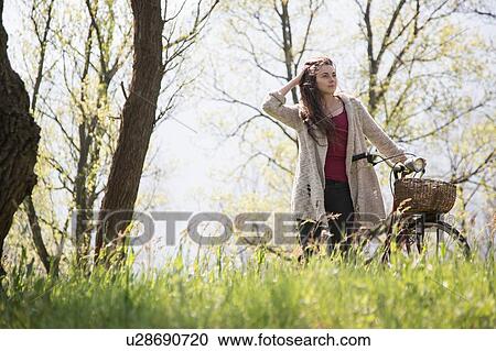 Stock Image - Young woman with bicycle in rural woodland. Fotosearch