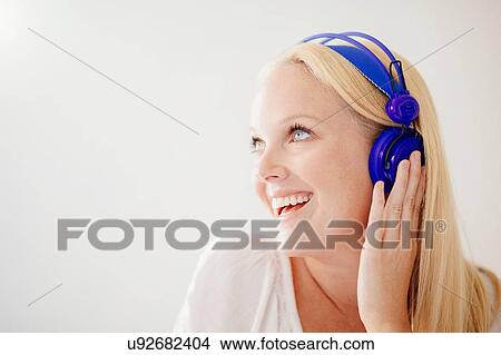 Picture - Young woman with long blonde hair wearing headphones looking away smiling. Fotosearch