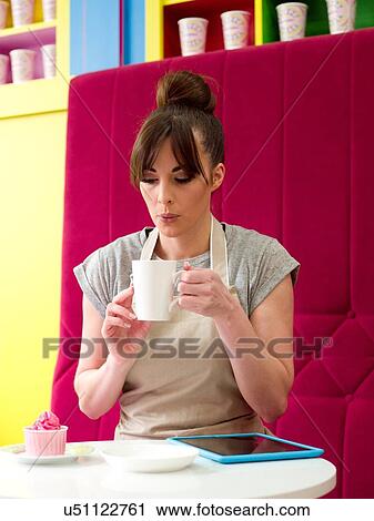 Stock Image - "Young woman, working in cake shop, taking coffee break". Fotosearch
