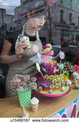 Stock Photo - "Young woman working in cake shop, arranging window display". Fotosearch