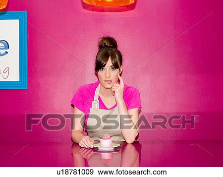"Young woman, working in cake shop, sitting with cupcake in front of her" View Large Photo Image Stock Photo - "Young woman, working in cake shop, sitting with cupcake in front of her". Fotosearch