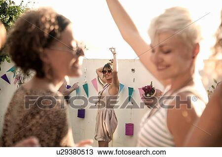 Stock Image - Young women chatting and dancing at poolside party. Fotosearch