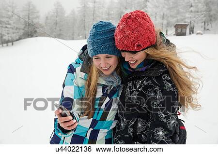 Stock Photograph - "Young women with smartphone smiling in snow, Sattelbergalm, Tirol, Austria". Fotosearch