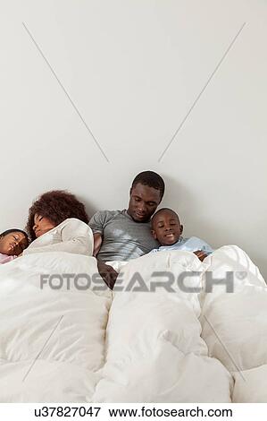 Stock Photo - African family sleeping in the bed togehter. Fotosearch