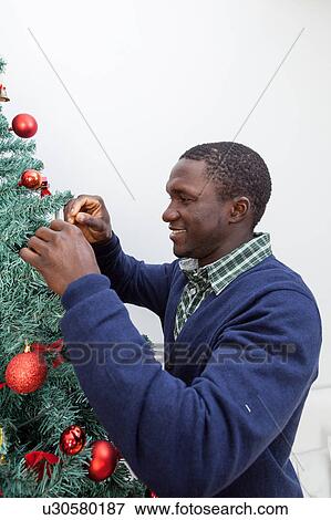 Stock Photo - Black man decorating the Christmas tree. Fotosearch