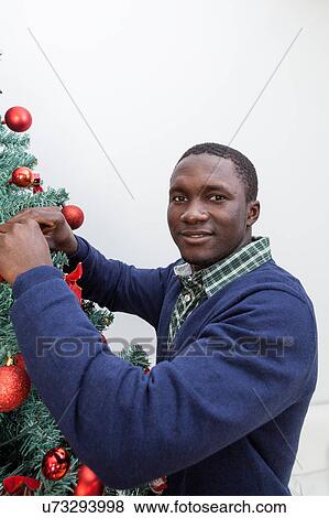 Stock Photo - Black man decorating the Christmas tree. Fotosearch