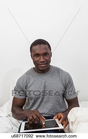 Black man looking at camera and touching his tablet View Large Photo Image Stock Image - Black man looking at camera and touching his tablet. Fotosearch
