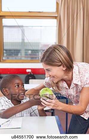 Stock Image - Boy giving to his teacher a apple. Fotosearch