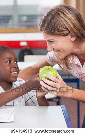 Stock Image - Boy giving to his teacher a apple. Fotosearch