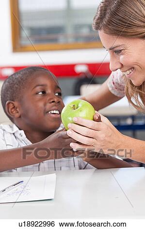 Stock Photograph - Boy giving to his teacher a apple. Fotosearch