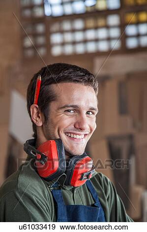 Stock Photo - Carpenter smiling with protectors hearing. Fotosearch