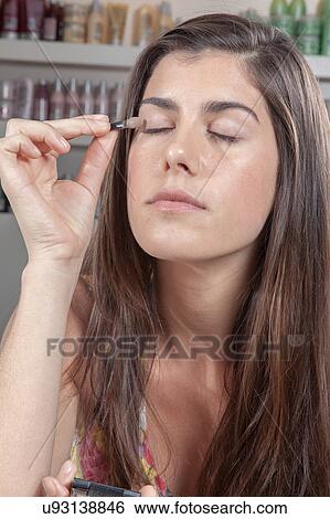 Stock Photograph - Concentrated woman applying eye shadow itself. Fotosearch