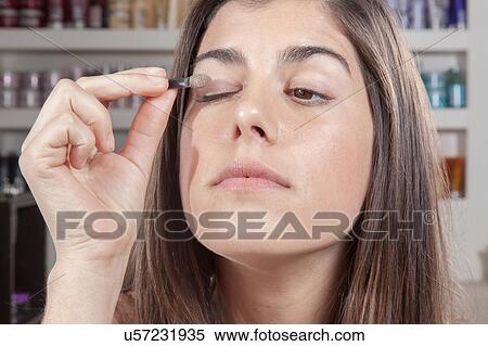 Stock Photography - Concentrated woman applying eye shadow itself. Fotosearch