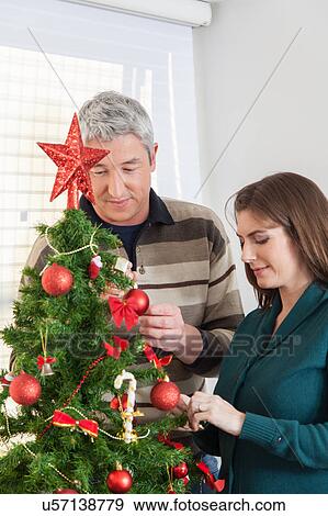 Stock Photo - Couple decorating christmas tree. Fotosearch