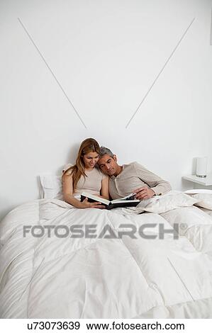 Stock Photo - Couple reading a book inside the bed. Fotosearch