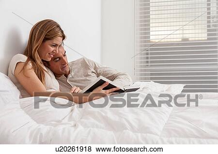 Stock Photo - couple reading a book lying in the bed. Fotosearch
