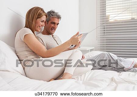 Stock Image - Couple using the ipad in the bed. Fotosearch
