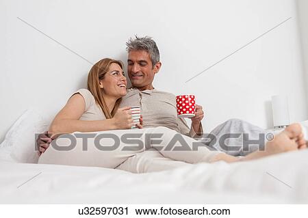 Stock Image - Happy couple drinking coffe in the bed. Fotosearch