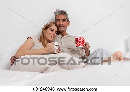 Stock Image - Happy couple drinking coffe in the bed. Fotosearch