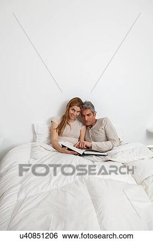 Stock Photograph - Happy couple reading a book inside the bed. Fotosearch