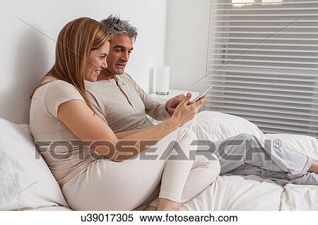 Happy couple using the ipad in the bed View Large Photo Image Stock Photography - Happy couple using the ipad in the bed. Fotosearch