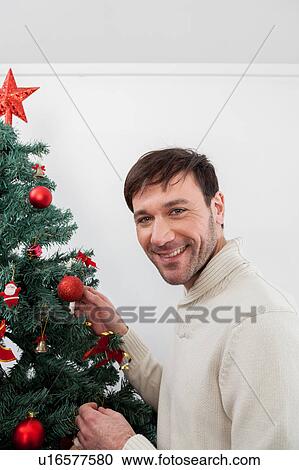 Stock Image - Happy man decorating the chrismas tree. Fotosearch