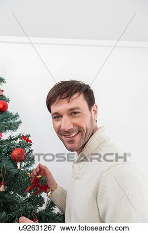 Stock Photo - Happy man decorating the chrismas tree. Fotosearch