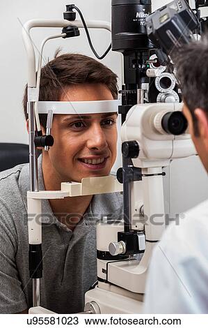 Stock Image - Happy man looking through the keratometer. Fotosearch