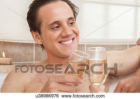 Stock Photograph - Happy man with champagne toasts in the bathtub. Fotosearch