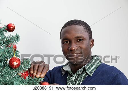 Stock Image - Man decorating the Christmas tree and looking at camera. Fotosearch