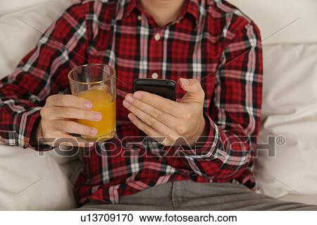 Stock Image - Man drinking a juice and checking his phone. Fotosearch
