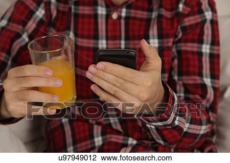 Stock Image - Man drinking a juice and checking his phone. Fotosearch