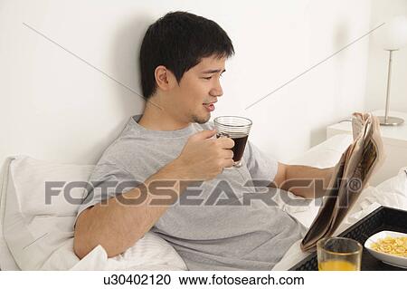 Stock Image - Man having a breakfast while reading the newspaper. Fotosearch