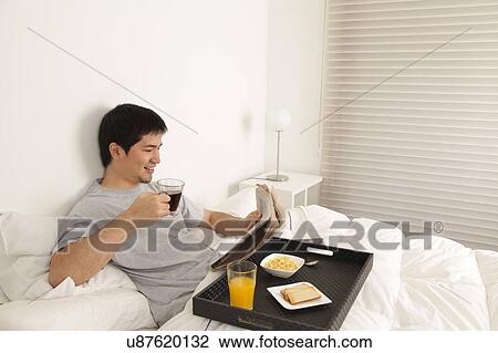 Stock Image - Man having a breakfast while reading the newspaper. Fotosearch