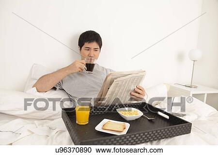 Stock Image - Man having a breakfast while reading the newspaper. Fotosearch