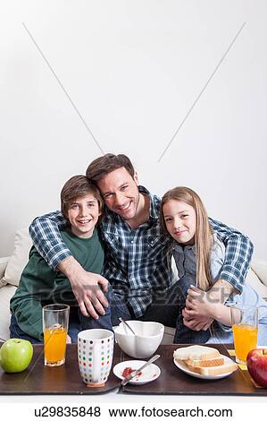 Stock Photo - Man having a breakfast with your two childrens. Fotosearch