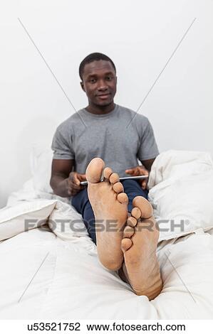 Stock Image - Man in feet in his bed checking his tablet. Fotosearch