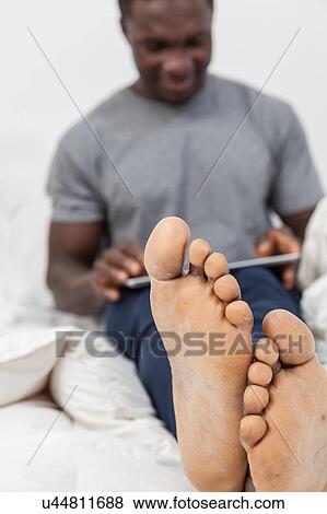 Stock Photo - Man in feet in his bed checking his tablet. Fotosearch